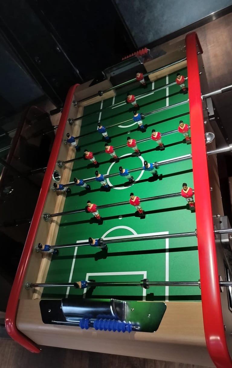 Foosball table with red frame and green playing surface with yellow and blue player figures on metal rods