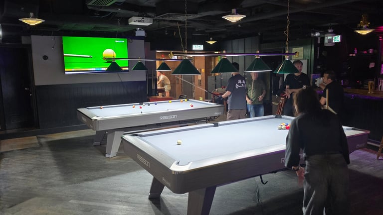 Indoor recreation room with two air hockey tables and people playing, sports displayed on green screen TV above